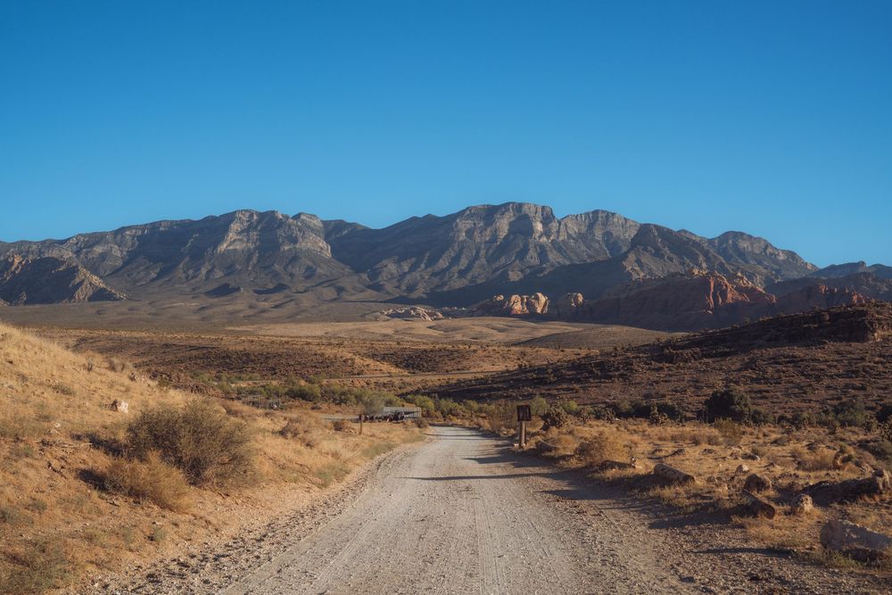 Dirt road winding through desert terrain with mountain ranges in the distance.