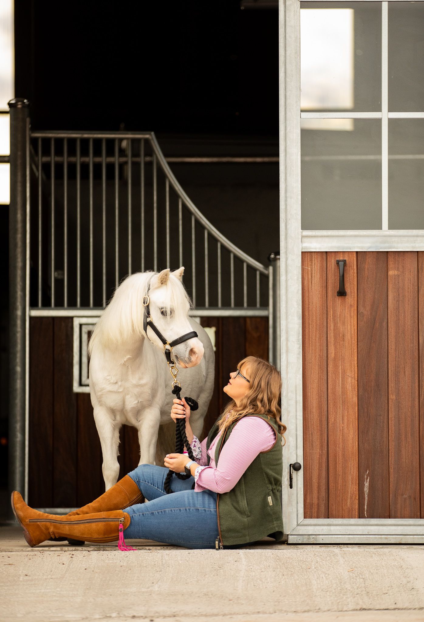 A brown horse and companion share tender moments in a sunlit garden surrounded by delicate white flowers and greenery.