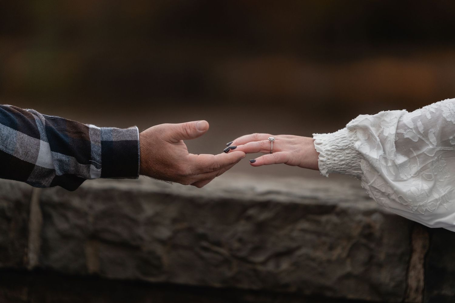 A close-up view of two hands exchanging a ring during a wedding ceremony against a dark background.