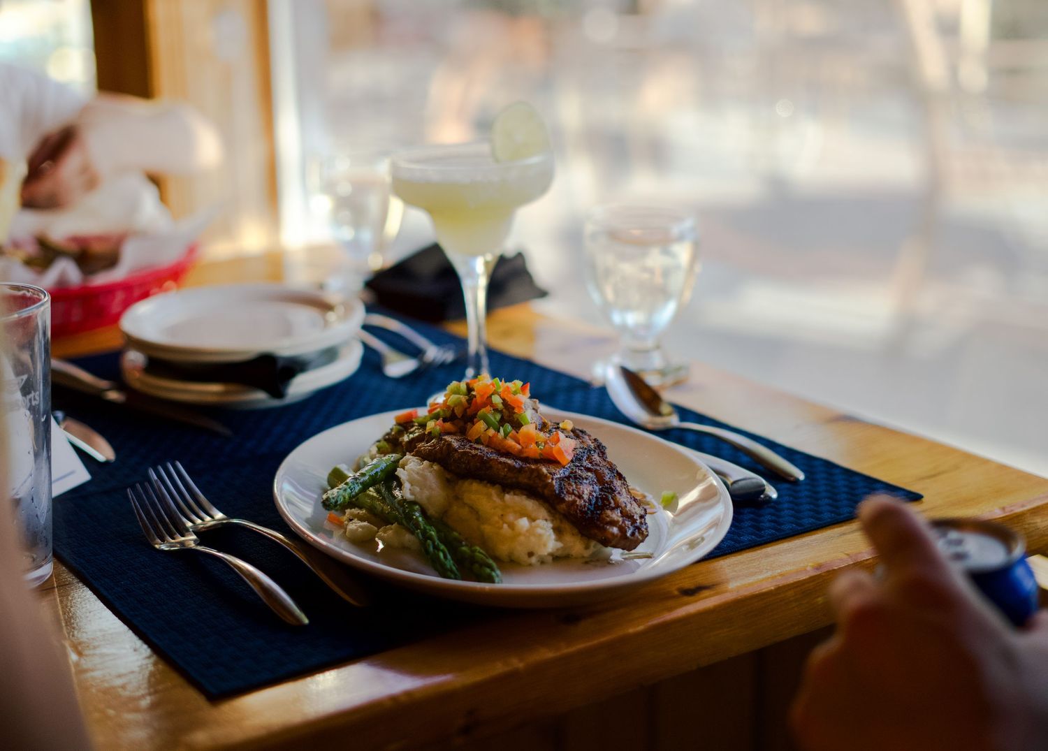 Elegant plated dinner with cocktail on blue placemats in restaurant setting.