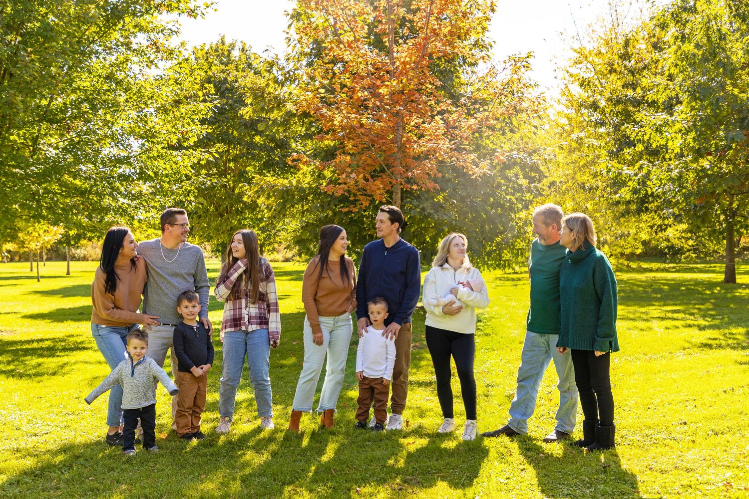 extended family at a park in the fall for a photo session with Elizabeth mayhew photography all looking at one another