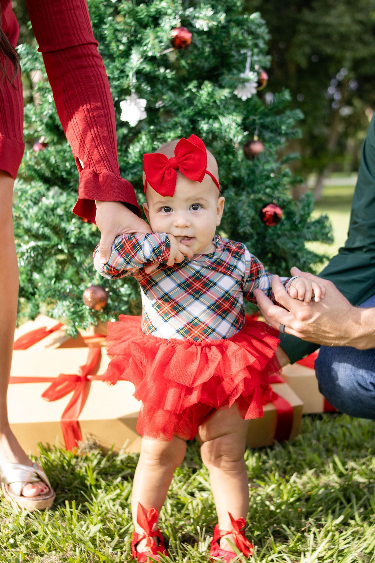 baby girl standing on grass smiling at camera christmas photo