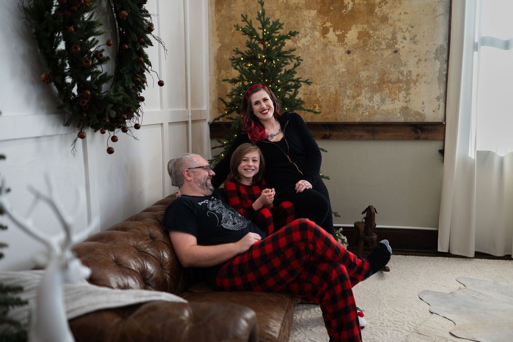 A festive holiday photoshoot in front of a Christmas tree with buffalo plaid decor and white decorations.