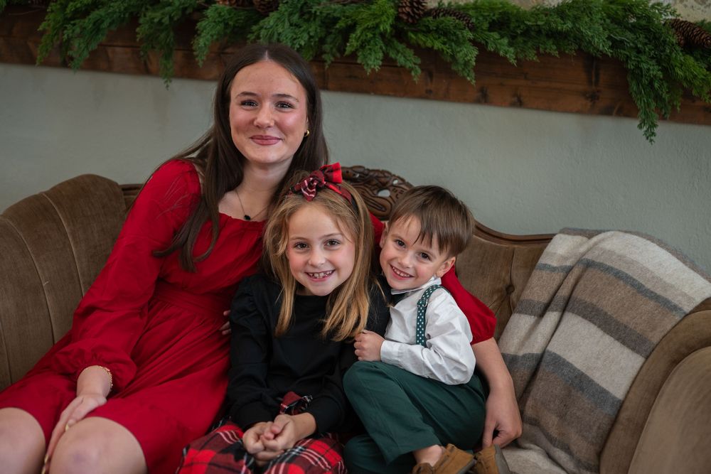 A family wearing red and green holiday outfits sits together on a couch for a festive portrait session.