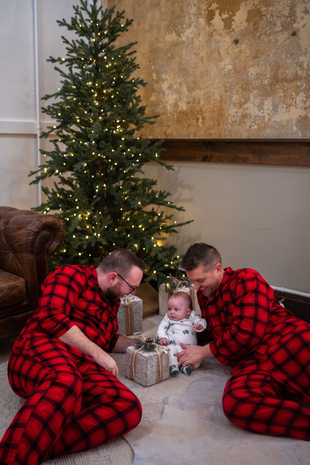 Family wearing matching buffalo plaid pajamas lying by Christmas tree and presents in cozy holiday scene.
