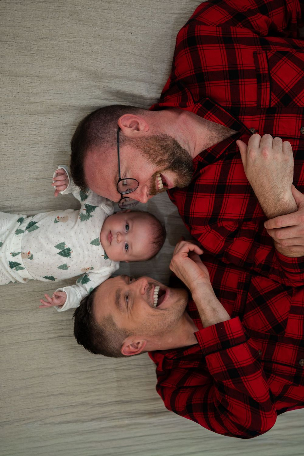 Two people in red plaid and white clothing lying down and laughing together on a light colored floor.