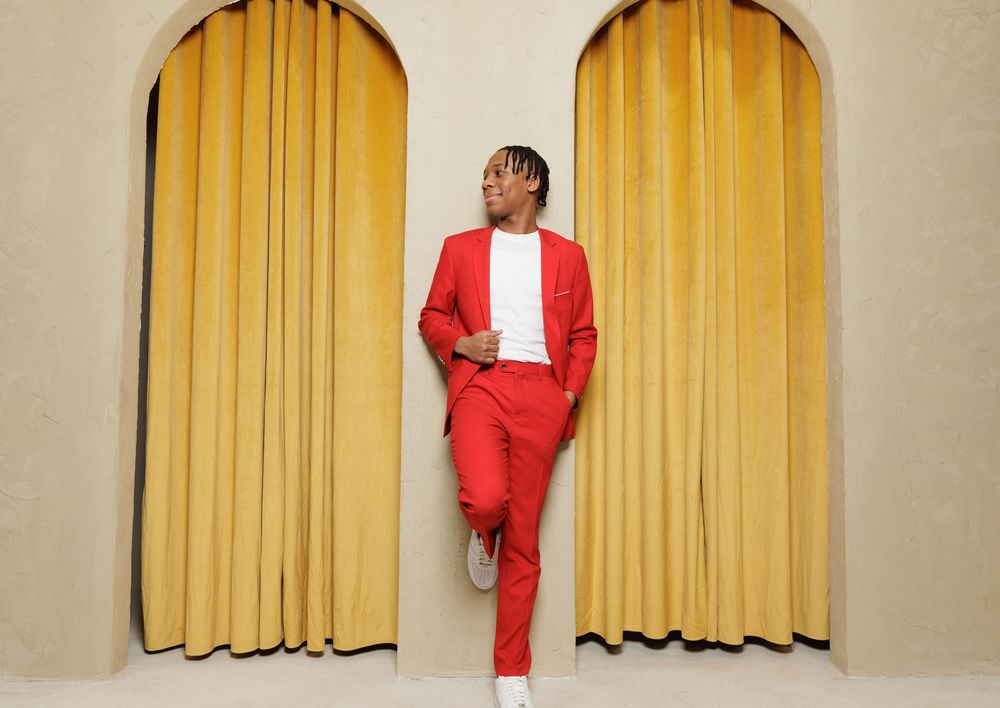 A figure in a red suit poses in front of a yellow curtain in a sequence of five similar shots.