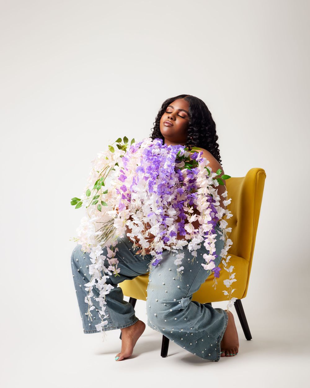 Artistic portraits with purple wisteria flowers draped over a yellow chair.