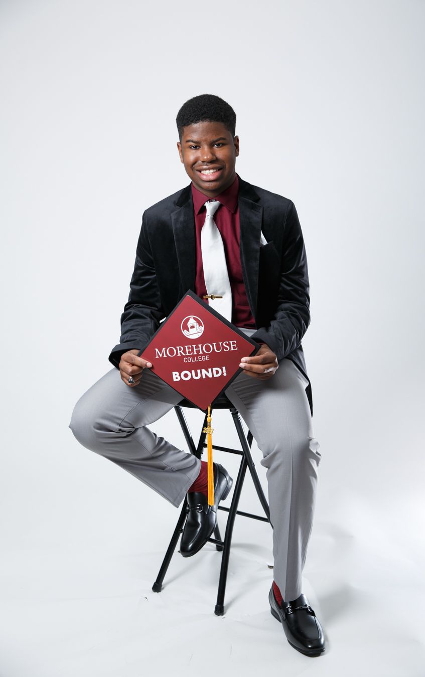 Student poses with Morehouse college sign wearing black blazer and gray slacks in professional studio setting.
