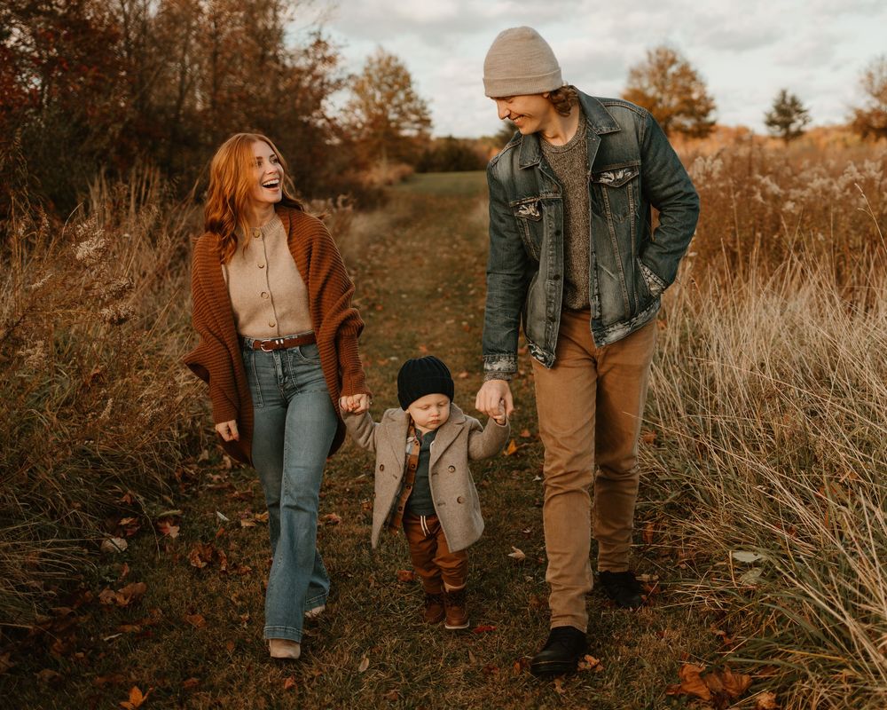 Family walking together through tall grass in autumn field at sunset.