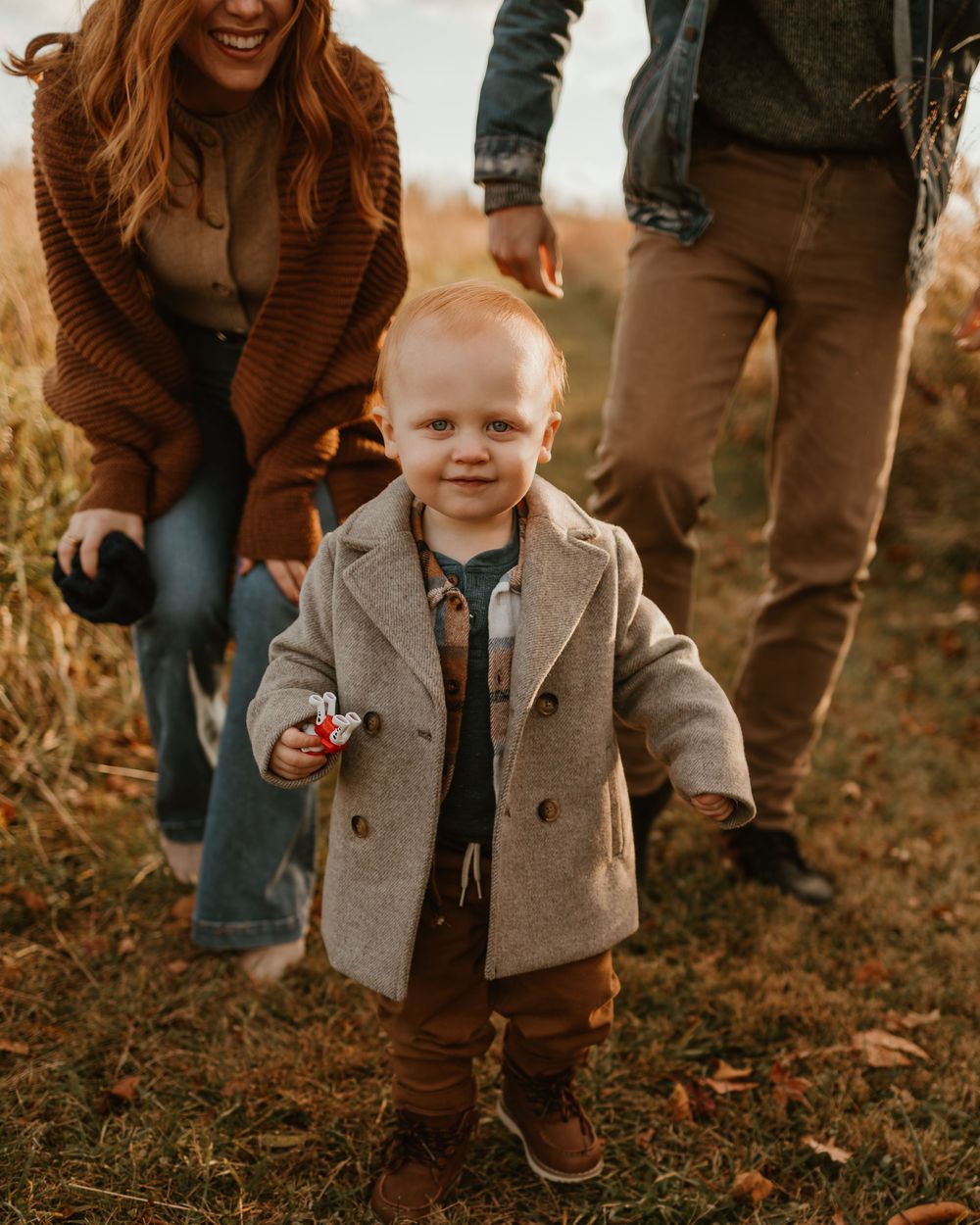 Child in gray coat walking through fallen leaves during autumn.