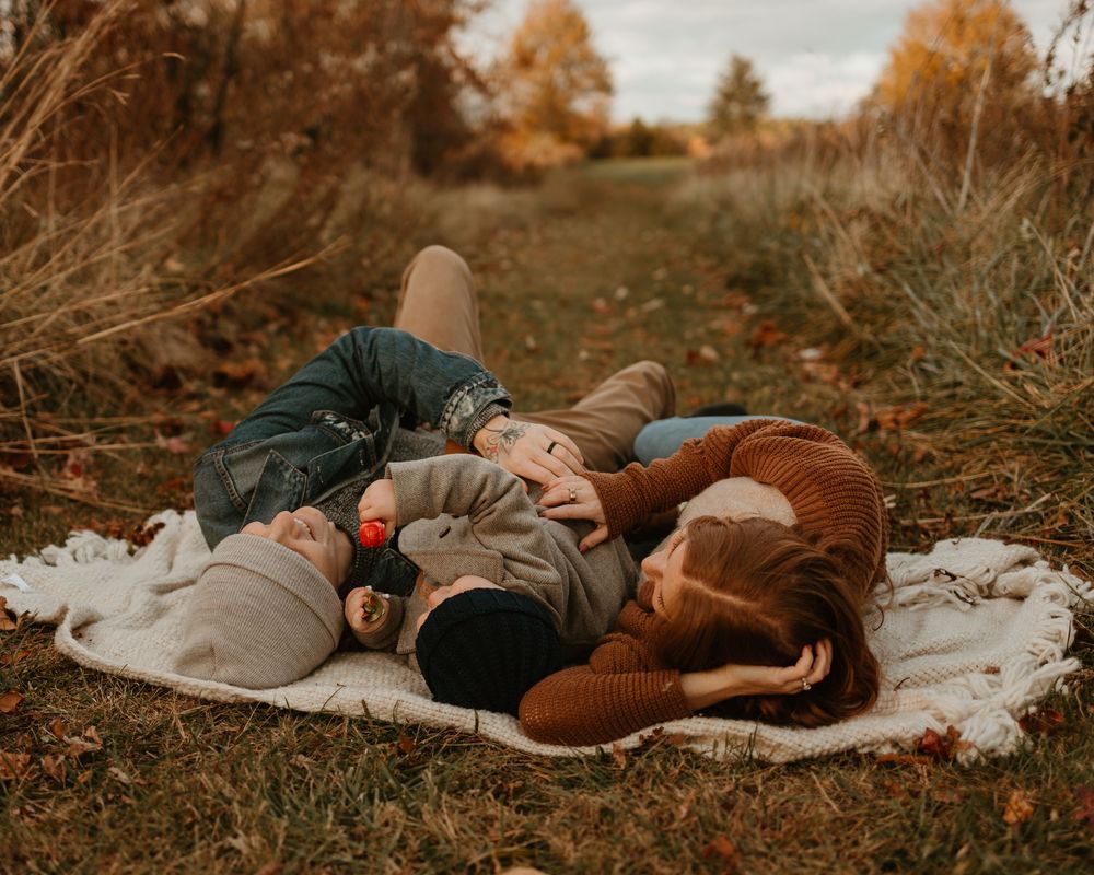 Cozy autumn photoshoot on a blanket outdoors with warm earth-toned sweaters and casual styling.