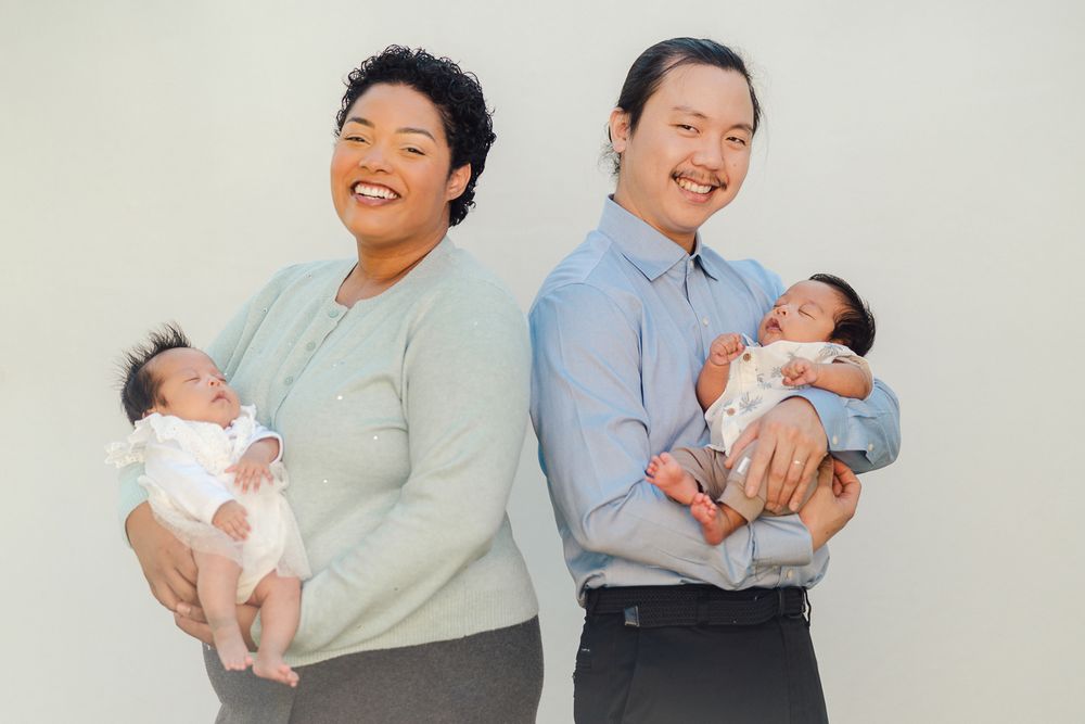 Parents and caregivers hold smiling babies wearing white outfits in a bright studio setting.