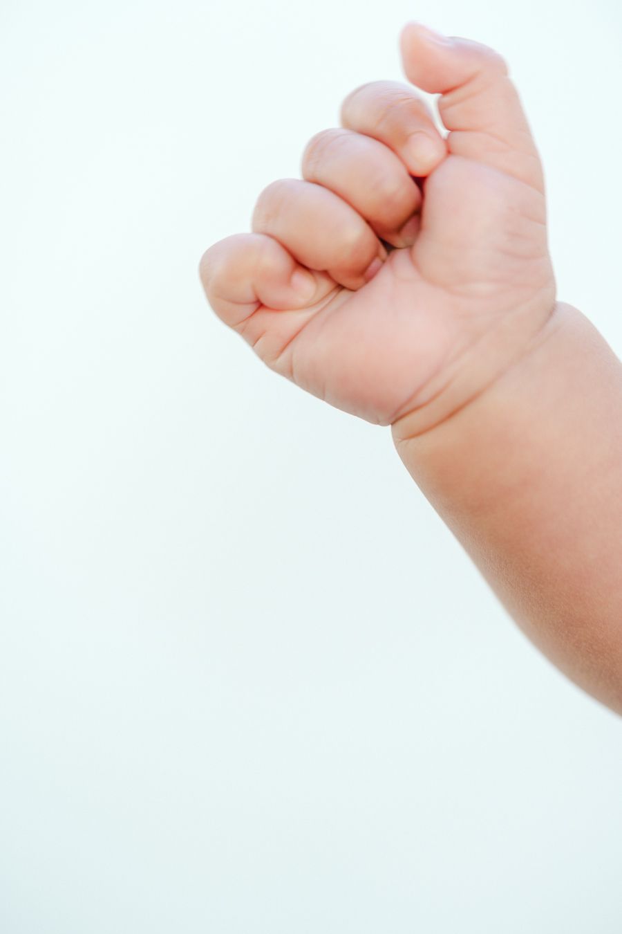 Close-up view of a tiny newborn baby's fist against a white background showing delicate skin and curled fingers.
