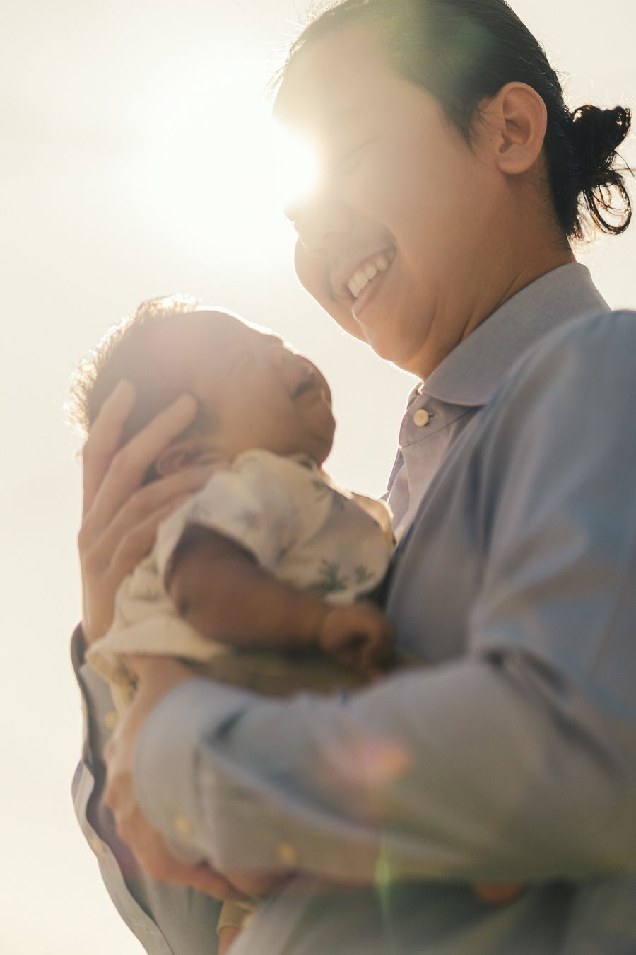 Silhouetted parent and baby share tender moment in warm backlit sunlight creating dreamy atmosphere.