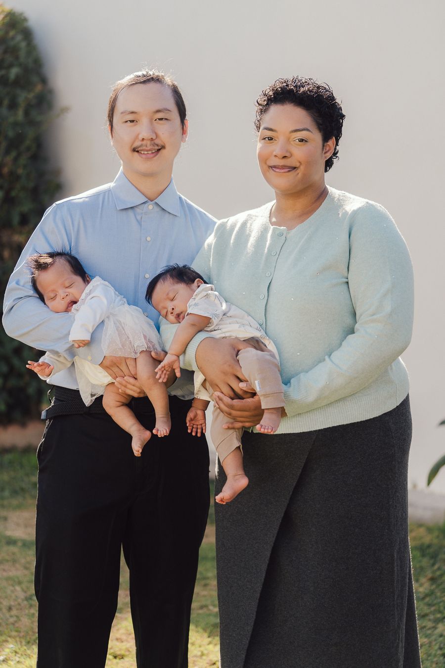 A couple in matching white tops and black pants hold their baby in a series of outdoor family photos.