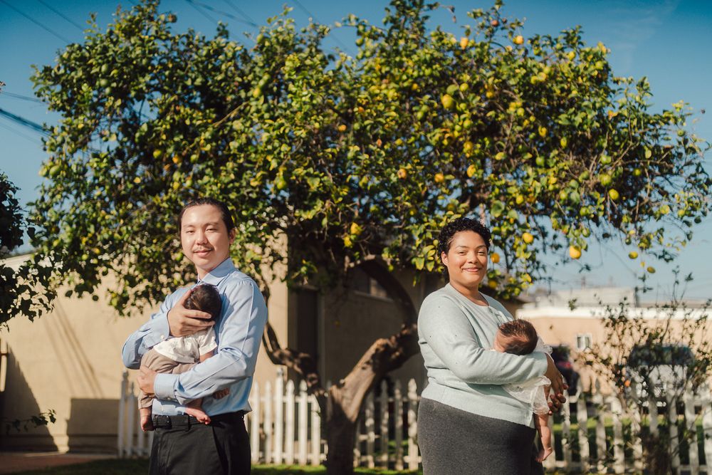 Parent and infant share loving cuddles in a backyard garden setting with green foliage and blue sky.