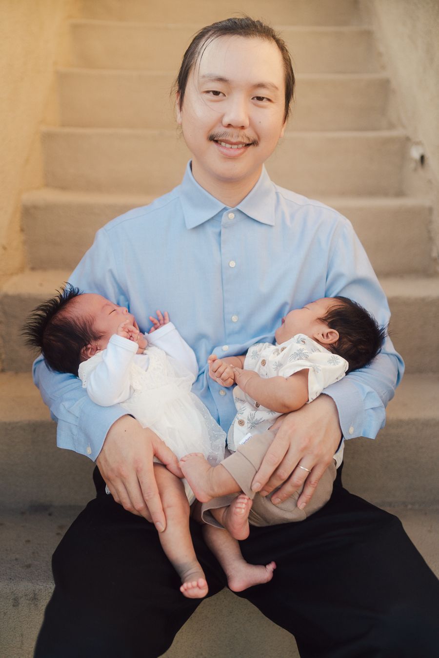 A series of photos showing someone in a light blue shirt sitting on steps while holding twin newborn babies in white outfits.