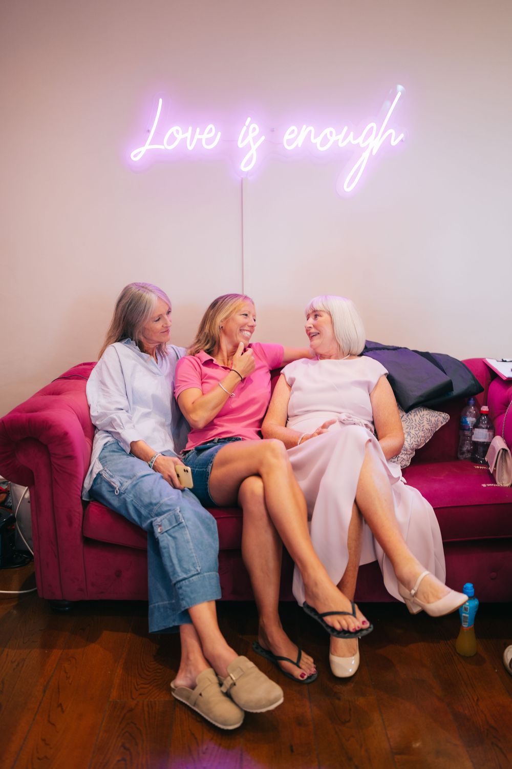 People relaxing on a pink couch under a neon sign in a dimly lit room at Pendrell Hall wedding venue