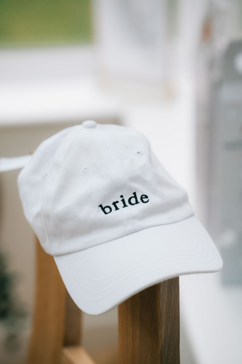 A white baseball cap with the word 'bride' embroidered in black text sits on a wooden surface  at Pendrell Hall wedding venue