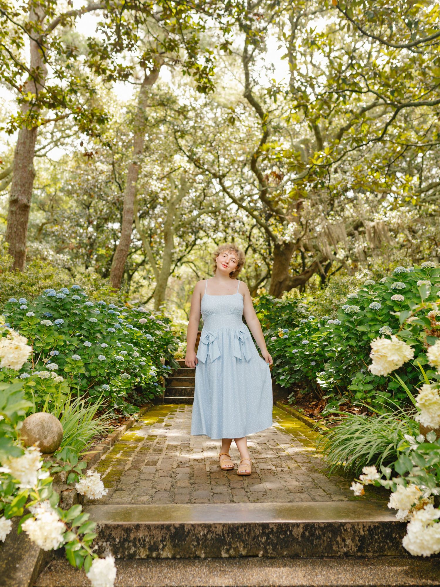 A light blue dress photographed in a garden setting with white hydrangea flowers and stone steps.