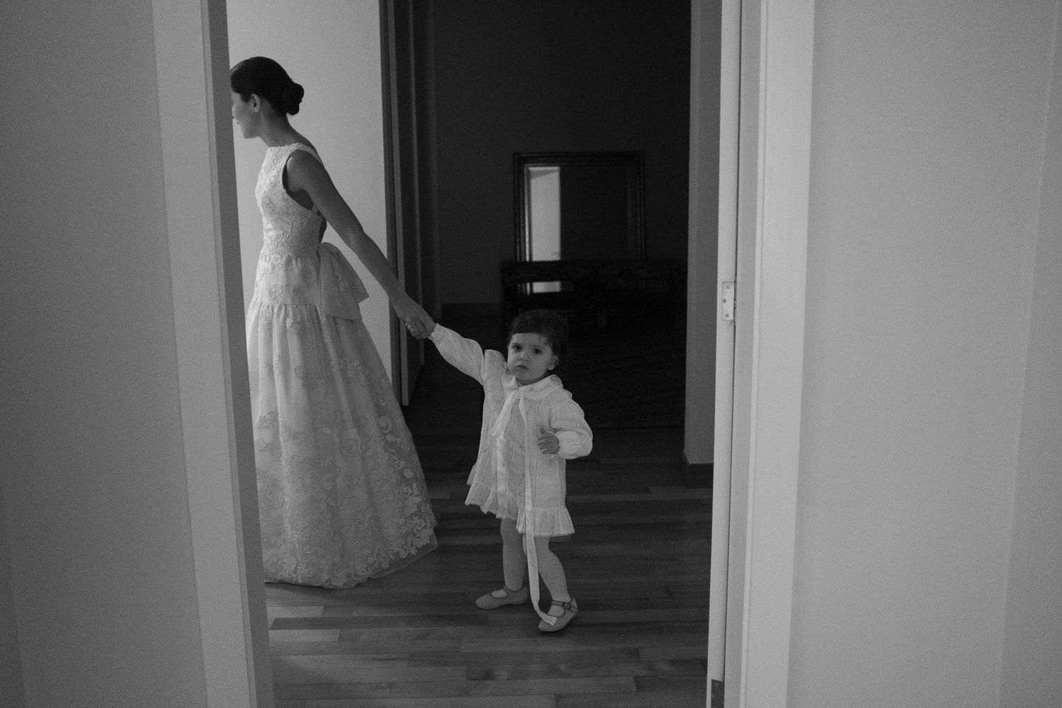 A black and white photograph shows a woman in a formal gown and small child in a white dress standing in a doorway.