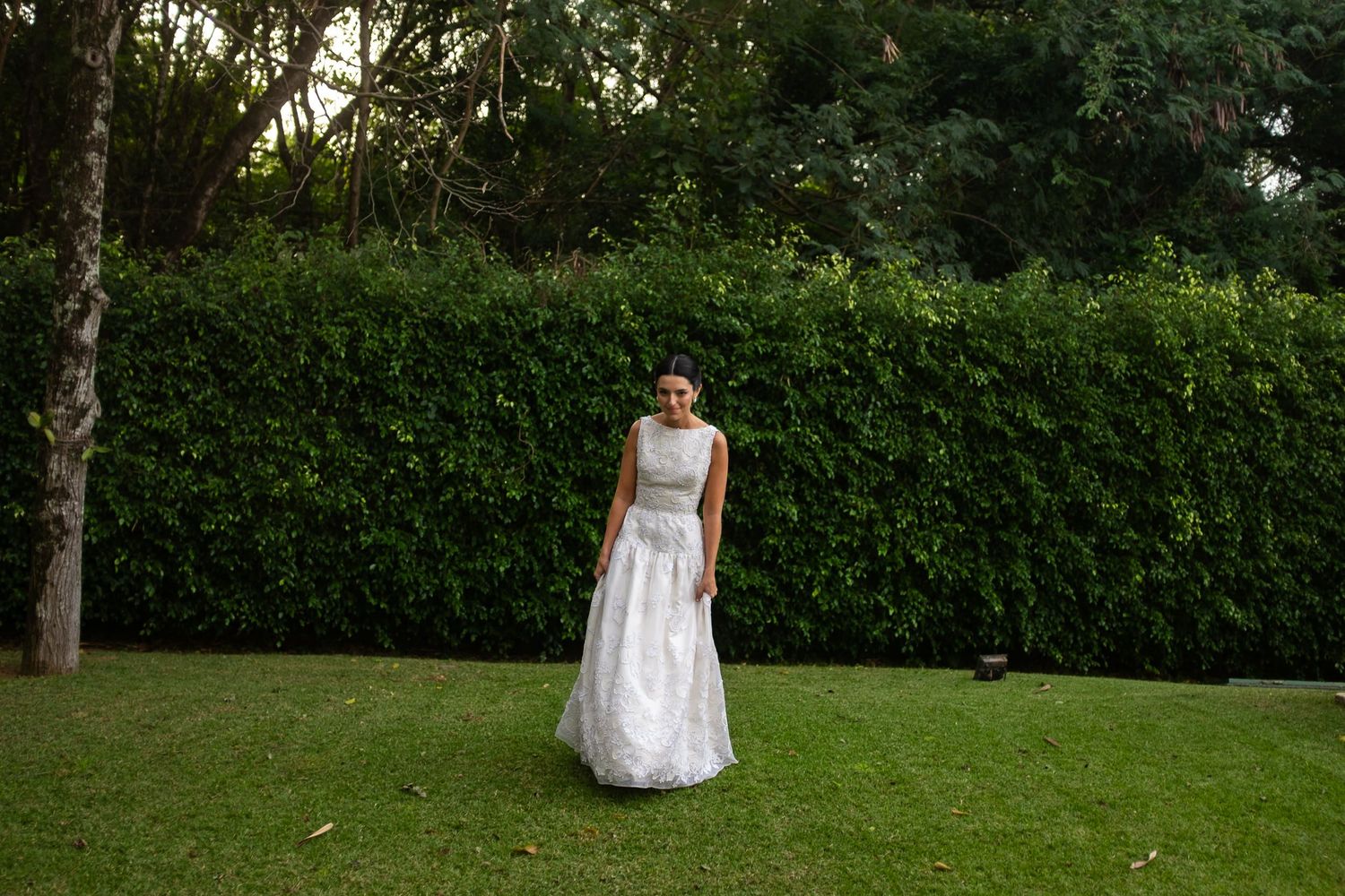 A white wedding dress is photographed against lush green garden foliage.