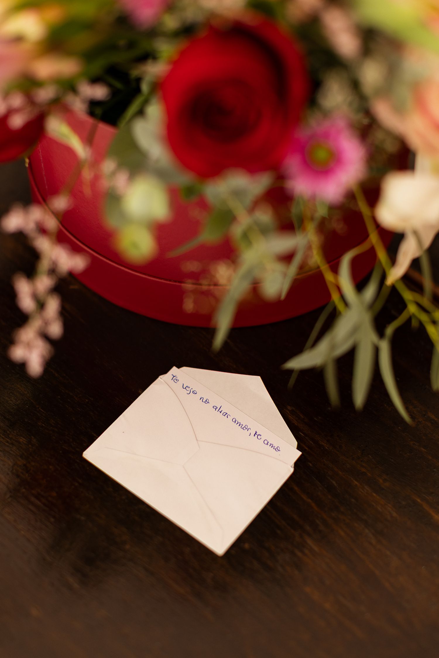 Red roses and pink flowers arranged with greenery above a handwritten note on dark wooden surface.