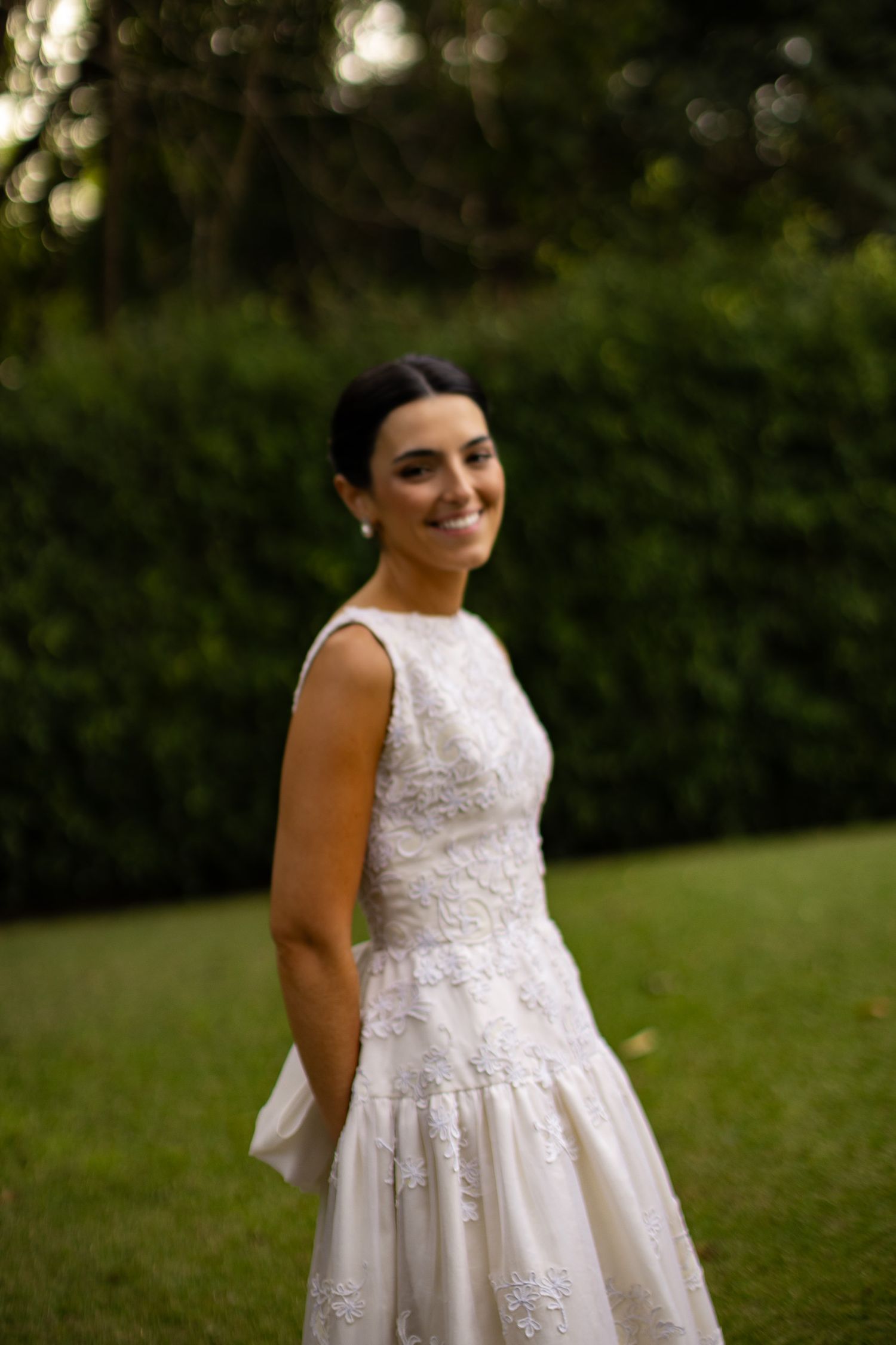 A beautiful white lace wedding dress with a sleeveless design is showcased outdoors against a natural green backdrop.