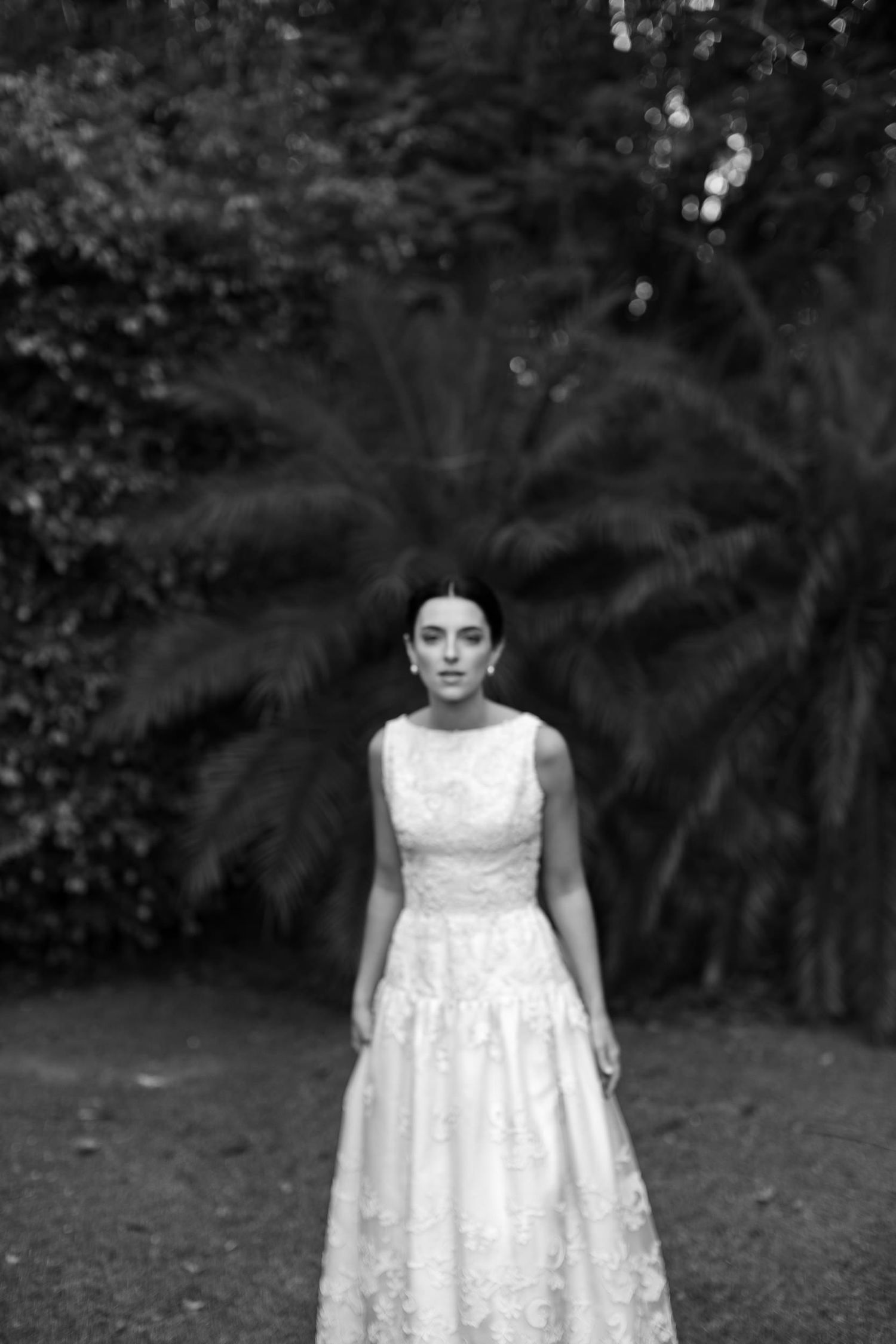A series of black and white photos showing a person in a white lace dress standing outdoors in a garden setting.