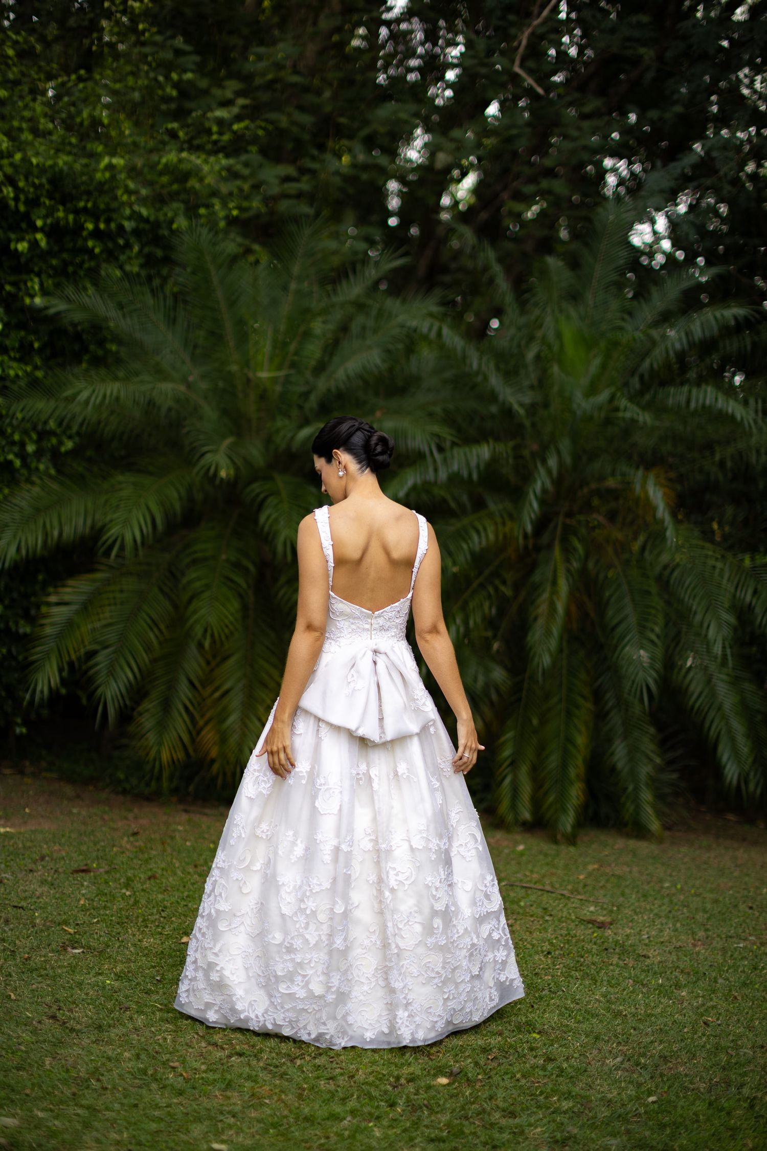A person in a white lace dress twirls in a garden setting with palm trees in the background.