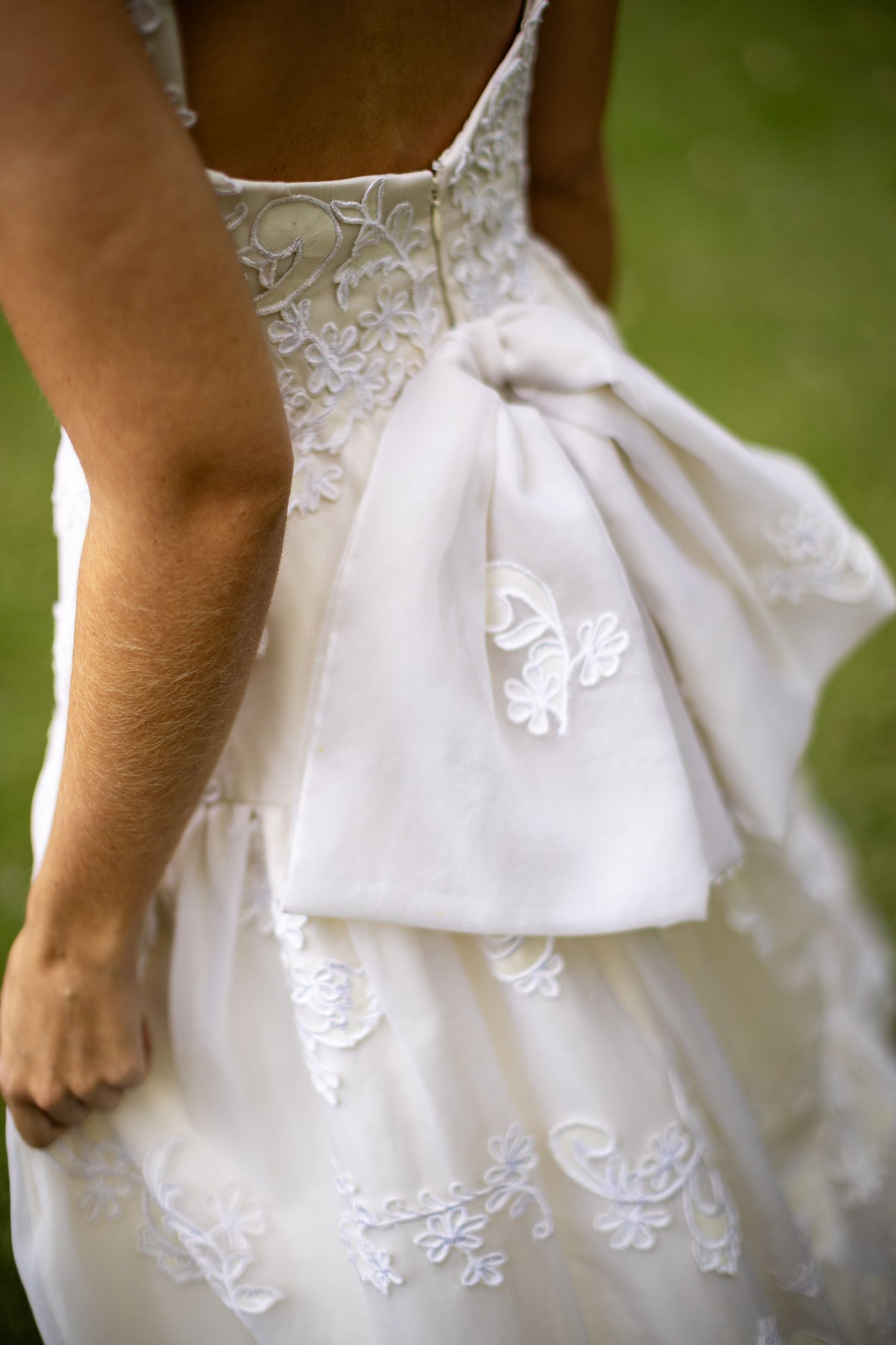 Close-up detail of white wedding dress with delicate butterfly lace embroidery and layered fabric design.