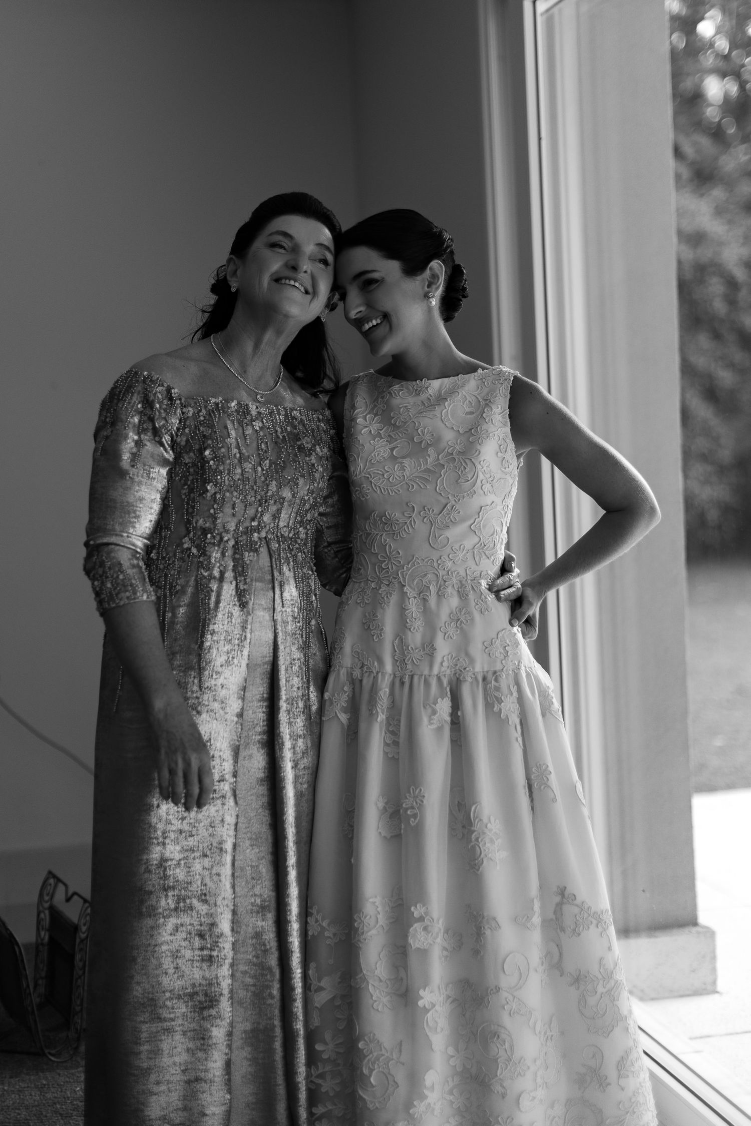 Two elegant white lace wedding dresses displayed side by side in natural window light.