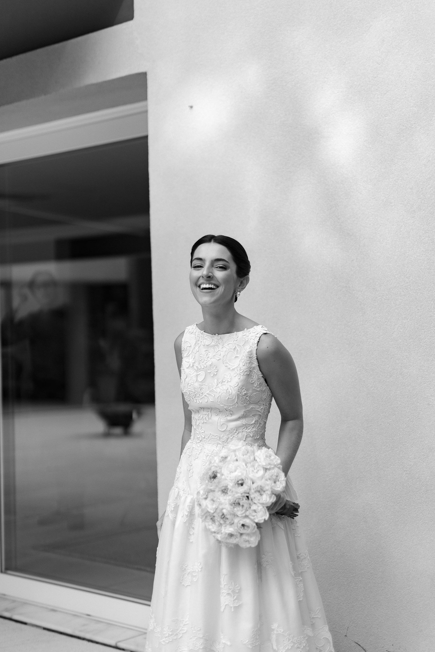A bride in a sleeveless white lace wedding dress poses in a black and white photo series.