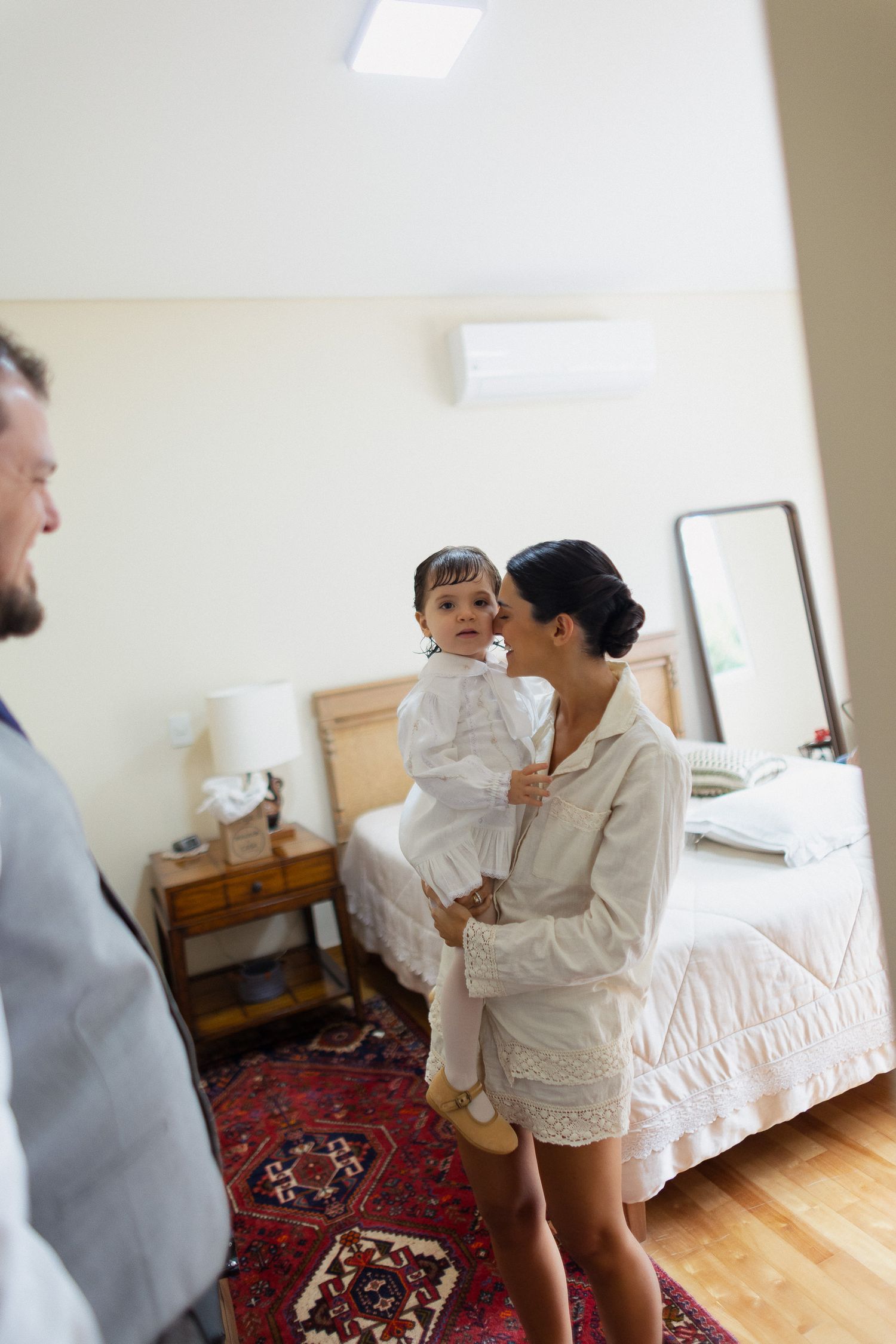 A family shares an intimate moment in a bedroom with hardwood floors and a decorative red rug.