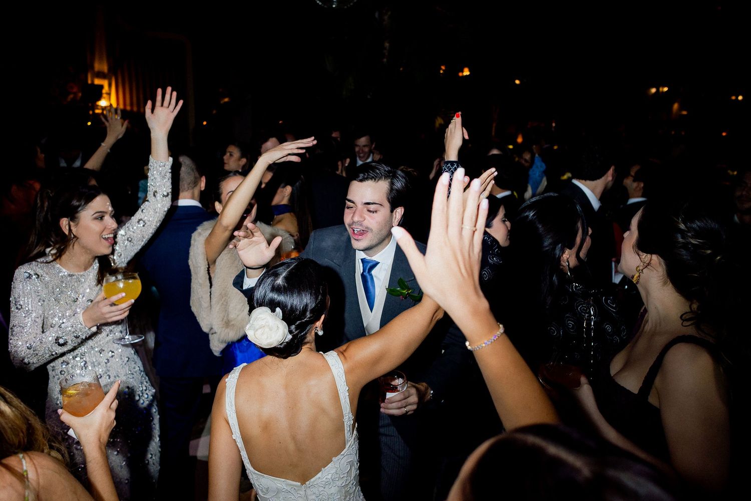 People dancing with raised hands on a dark dance floor at a lively party celebration.