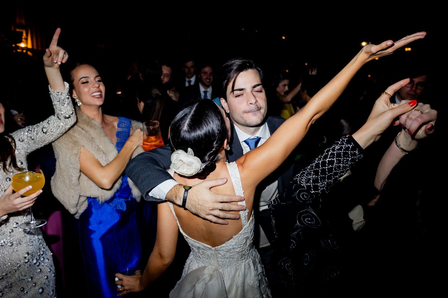 People dancing and celebrating at a lively party with raised arms and joyful expressions in a dark room.