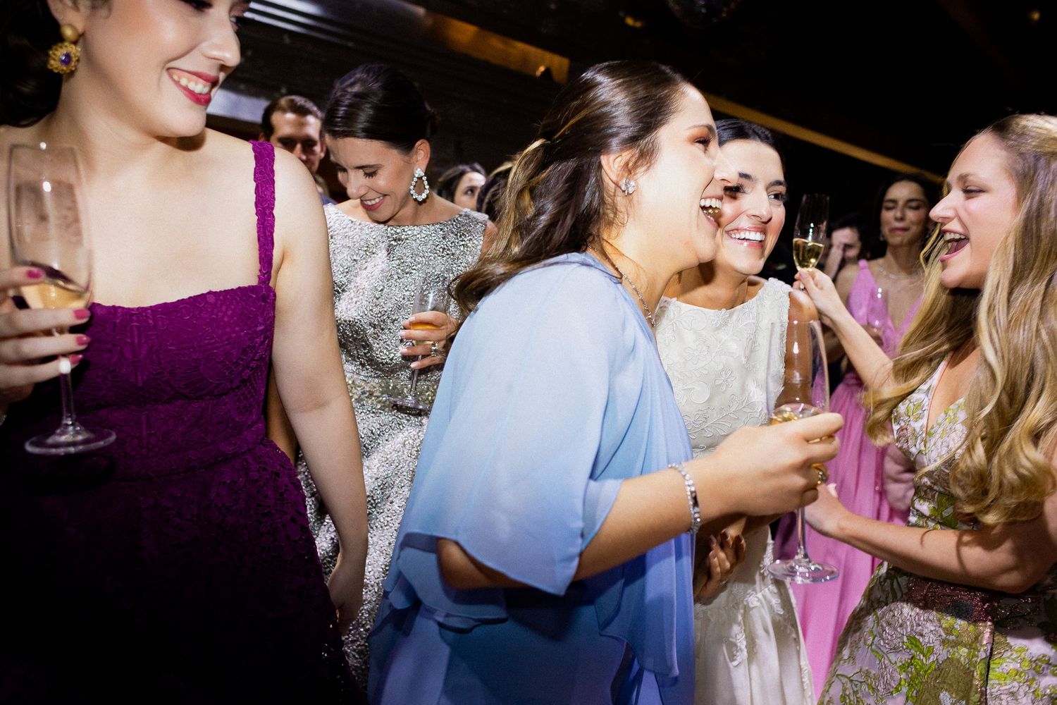 A group of people laughing and celebrating together at a social gathering with drinks in hand.