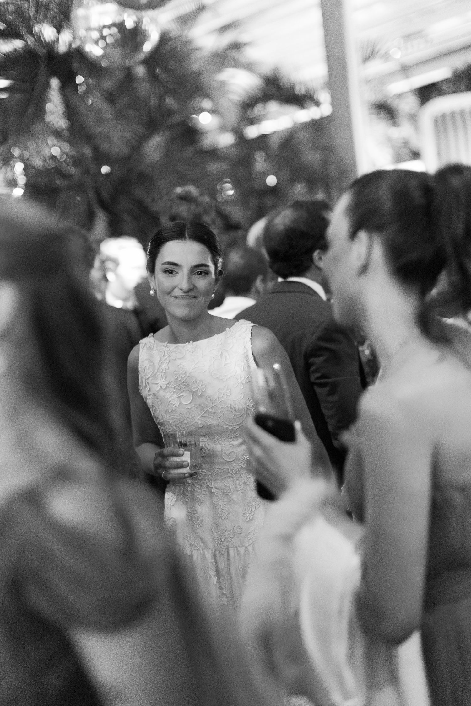 A bride in a white lace dress stands among wedding guests at an elegant reception.