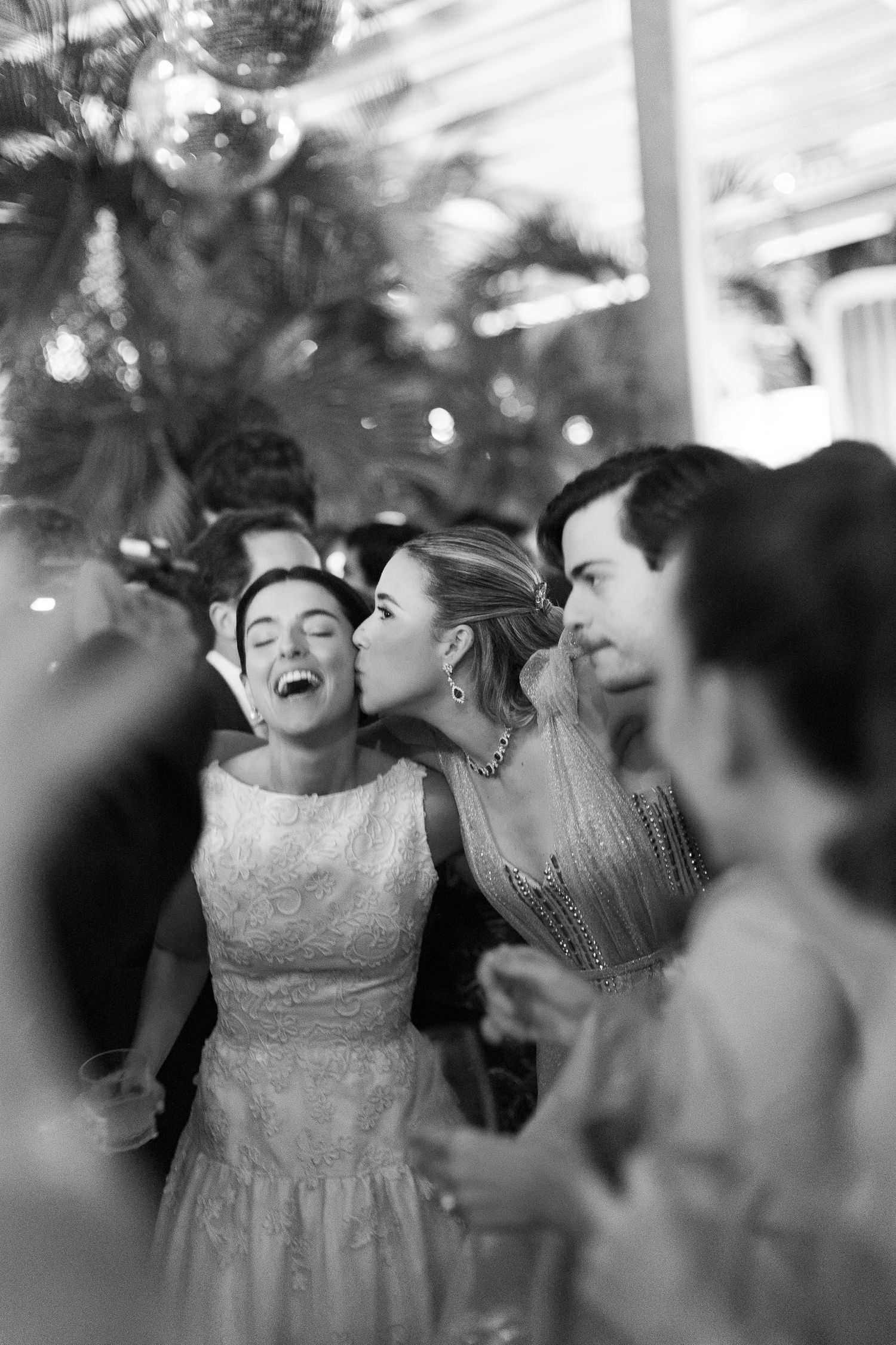 Black and white candid photo of joyful wedding celebration with guests laughing and sharing an intimate moment at reception.
