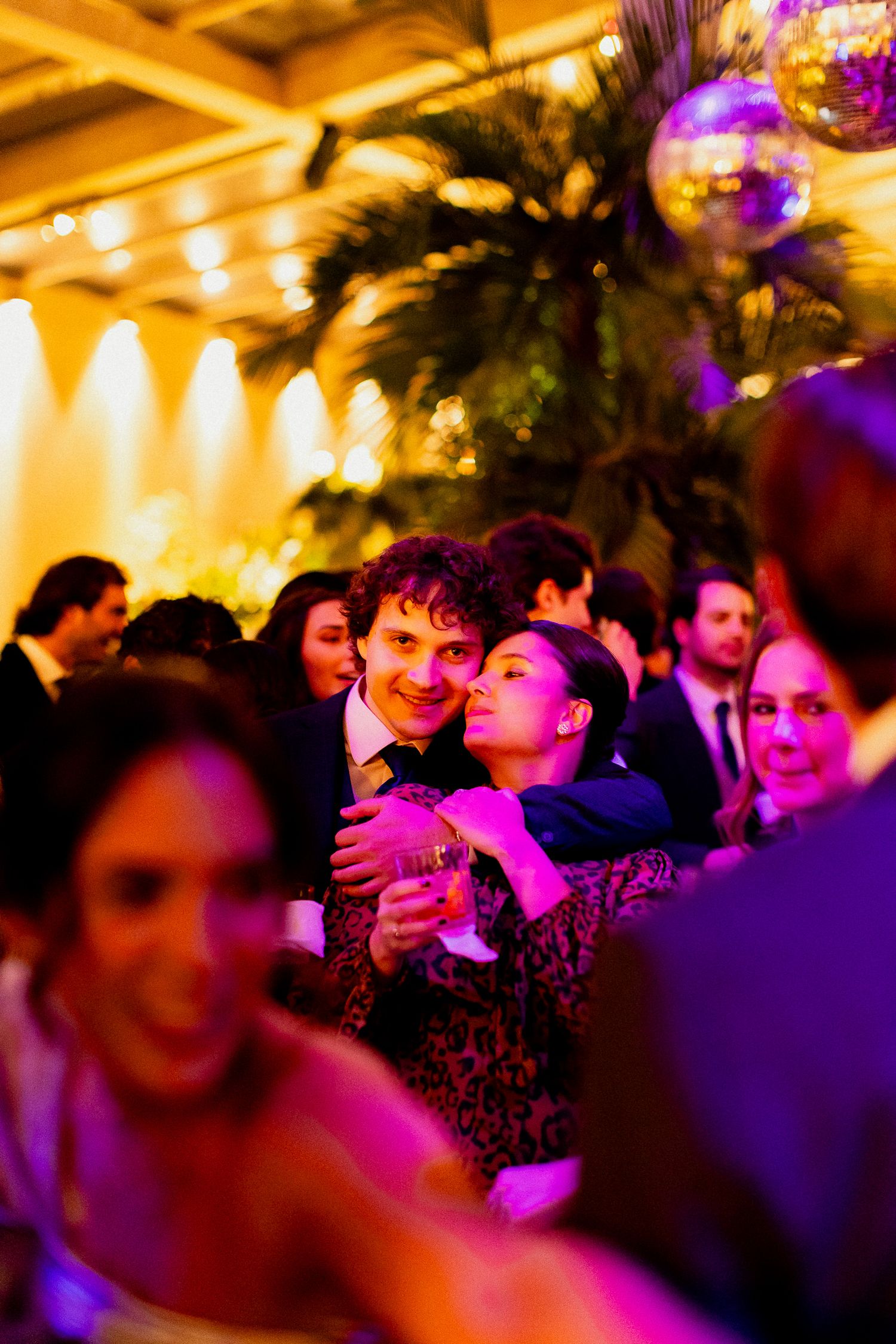 Crowded dance floor at a party illuminated by warm yellow and purple lighting creating a vibrant nightlife atmosphere.
