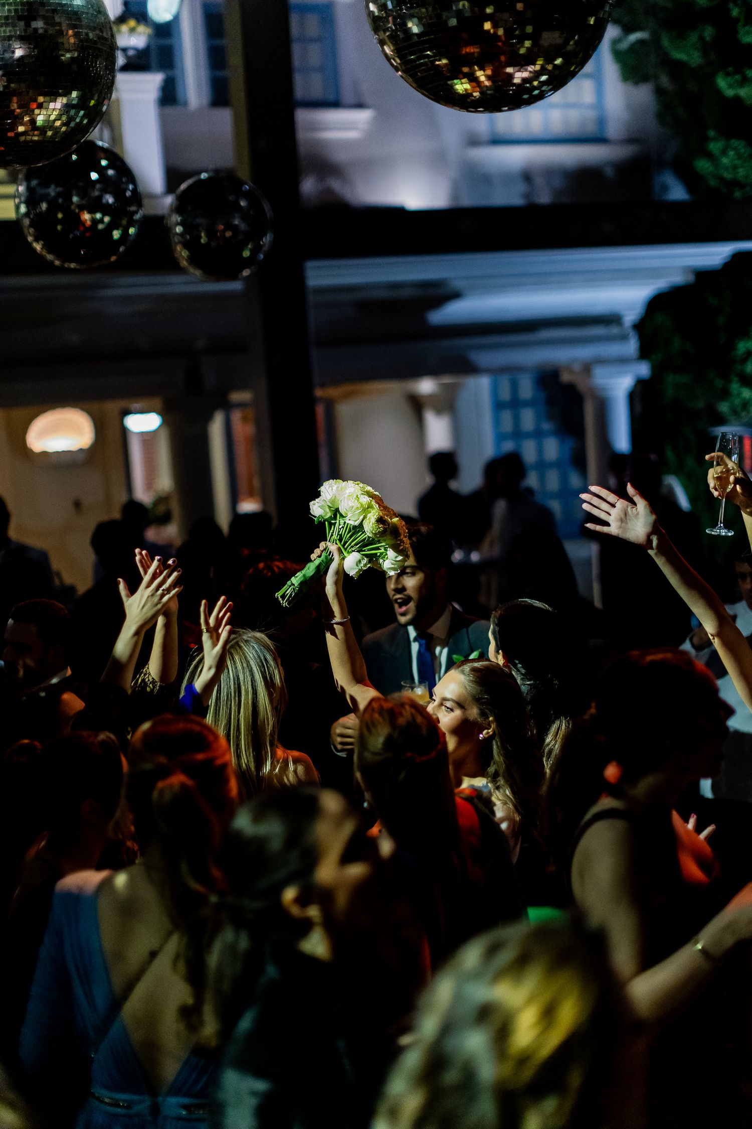 A crowd of people dancing and raising their hands at a nighttime party with disco ball lighting.
