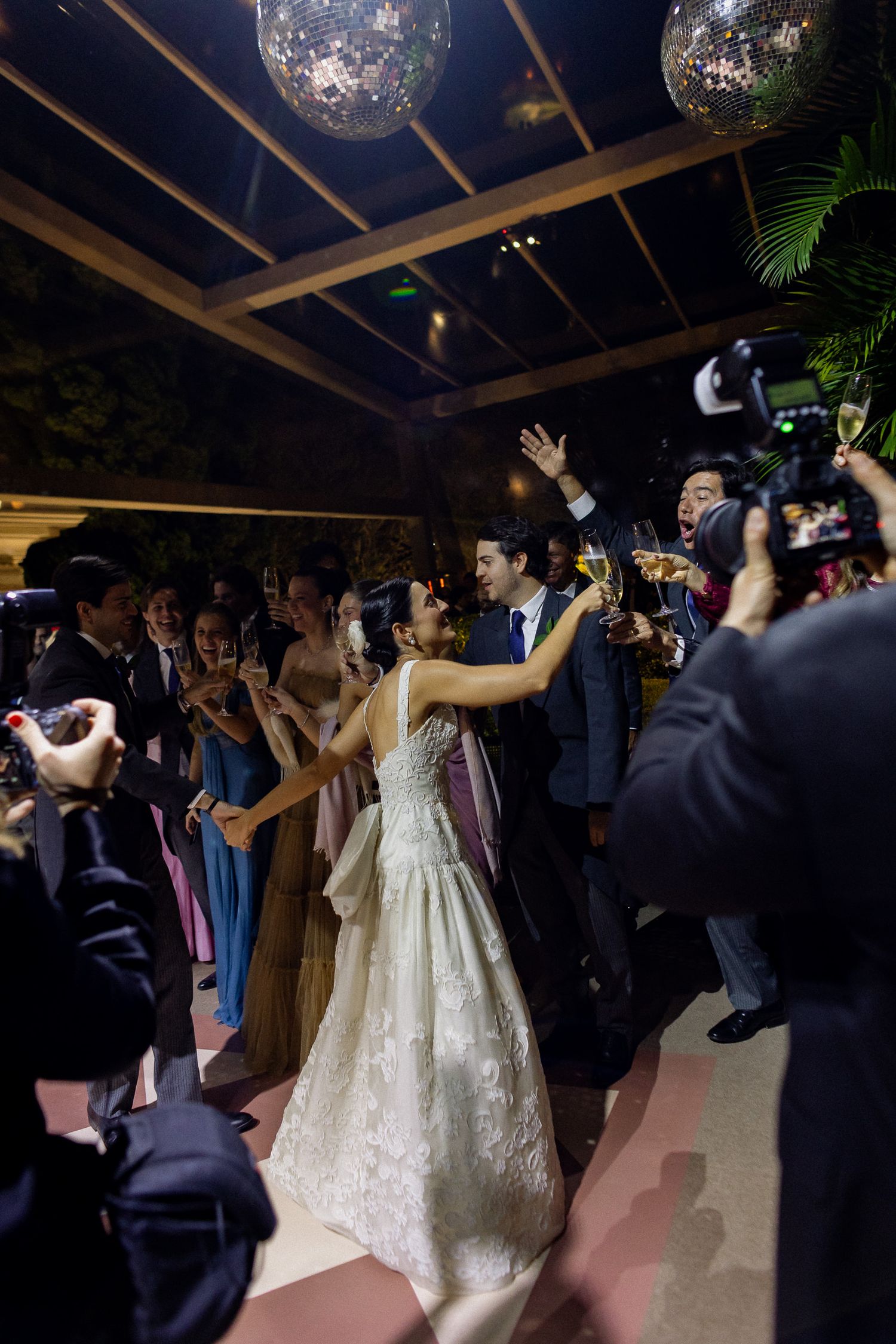 Wedding guests dance under disco balls and string lights at an elegant indoor reception celebration.