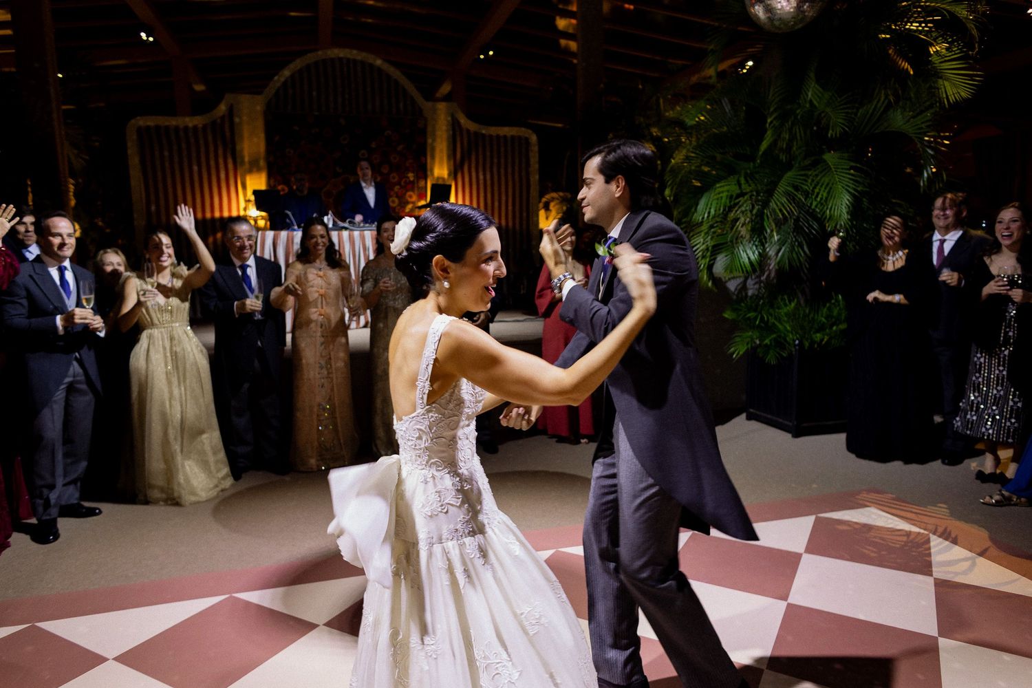 Wedding guests dance together on a checkered dance floor during an evening reception celebration.
