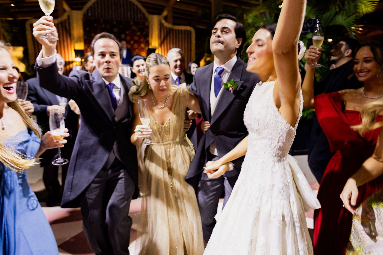 A joyous celebration at a wedding reception with guests raising champagne glasses and dancing in formal attire.