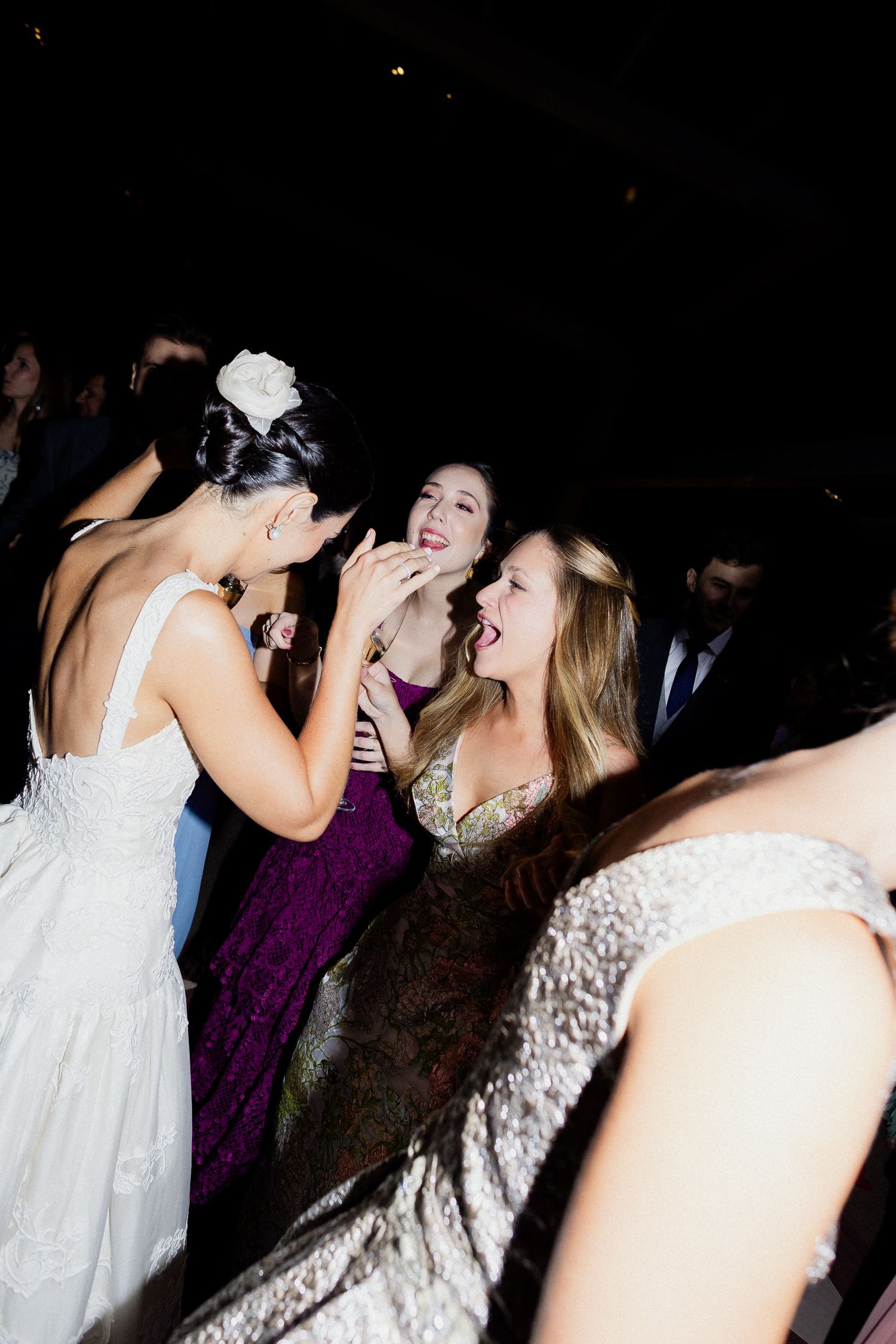 People in formal attire dancing and laughing together at a wedding reception celebration.