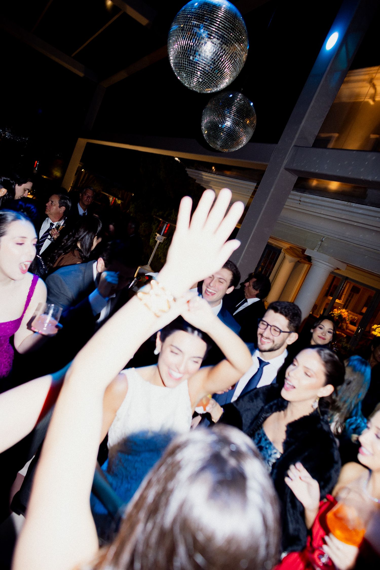 Energetic partygoers dancing and celebrating under a disco ball in a dimly lit venue.