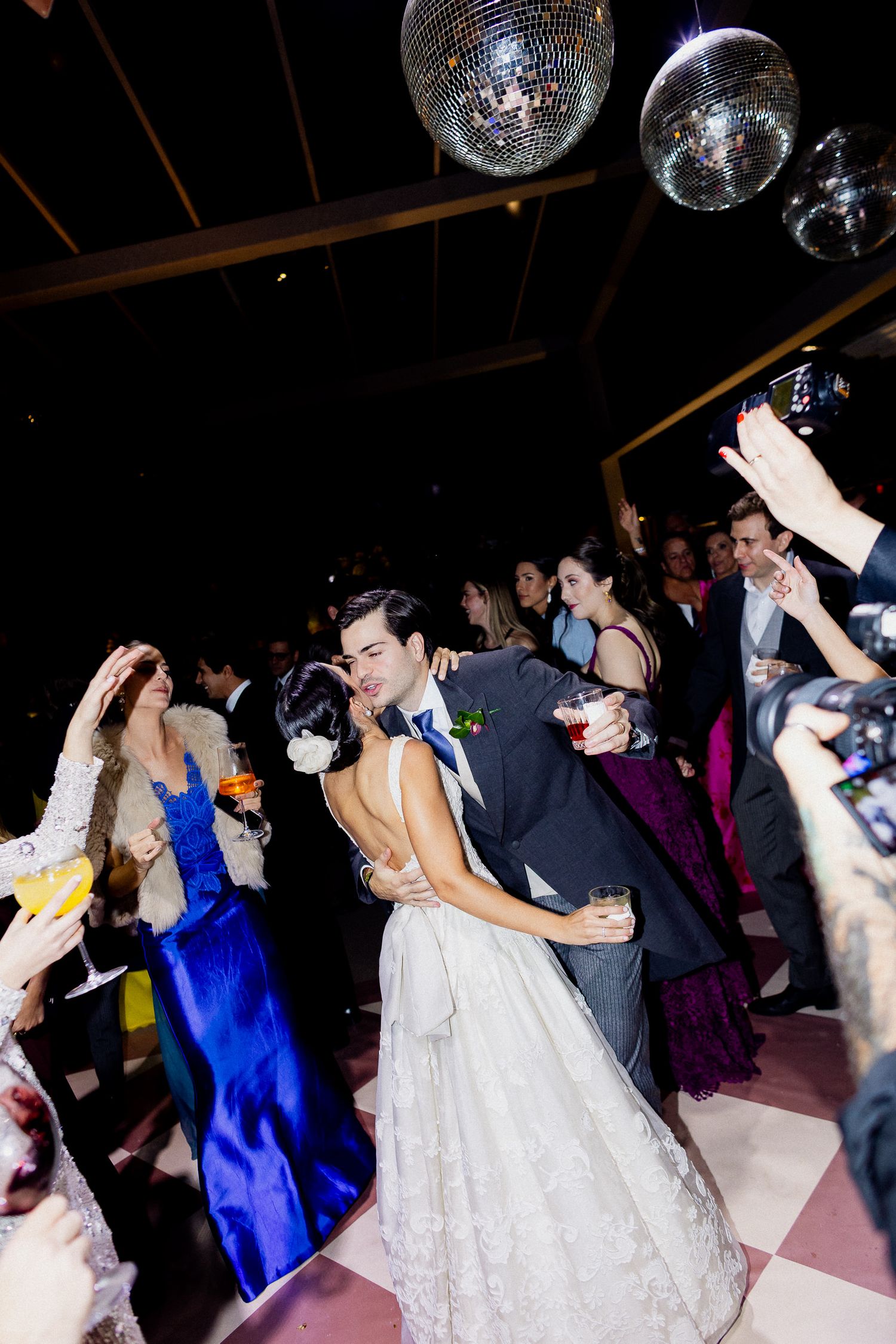 Couples dance under sparkling disco balls at an elegant wedding reception with guests in formal attire.