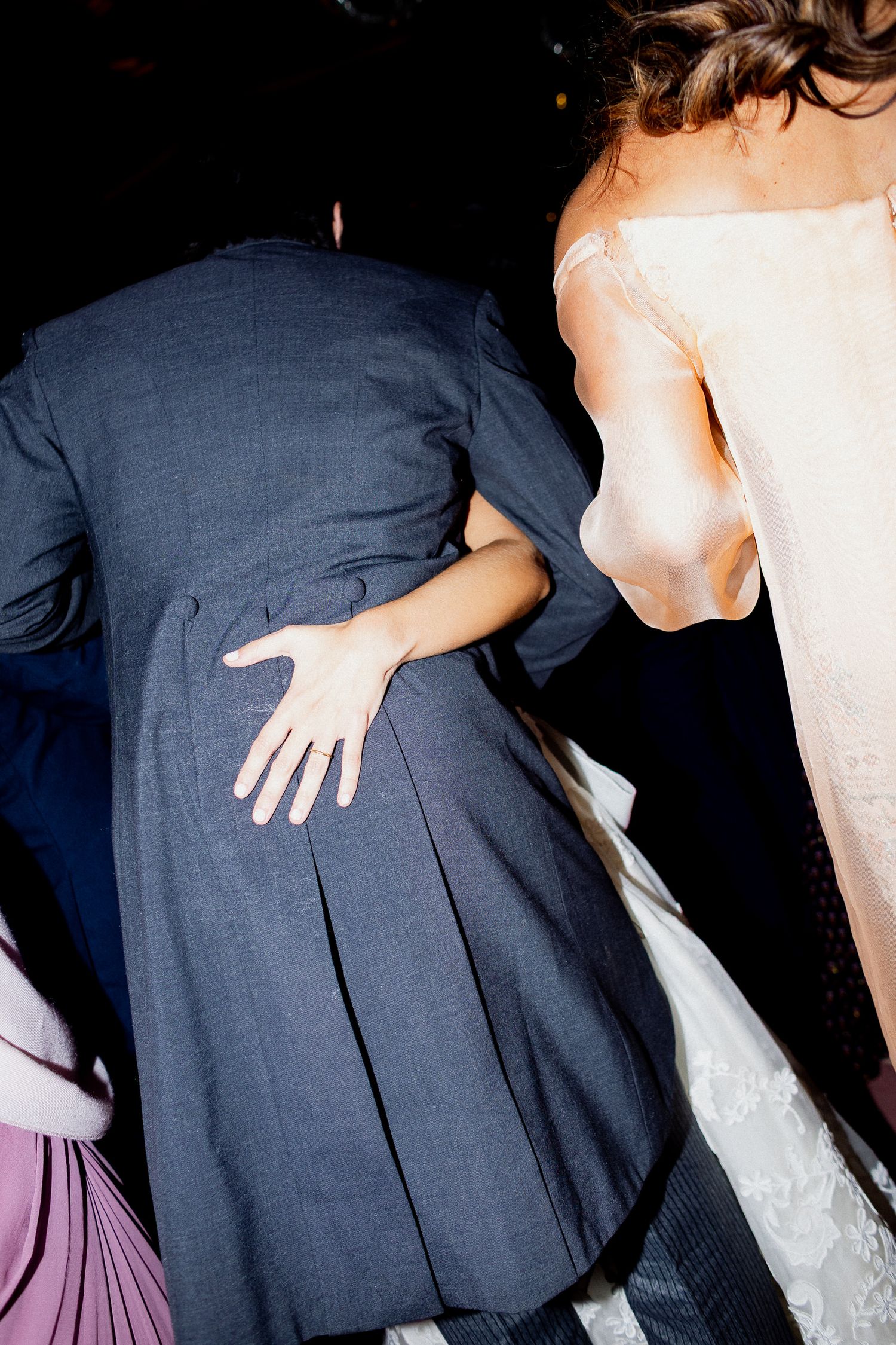 Close-up detail shots of wedding attire showing navy suit jackets and a white lace dress during candid moments.