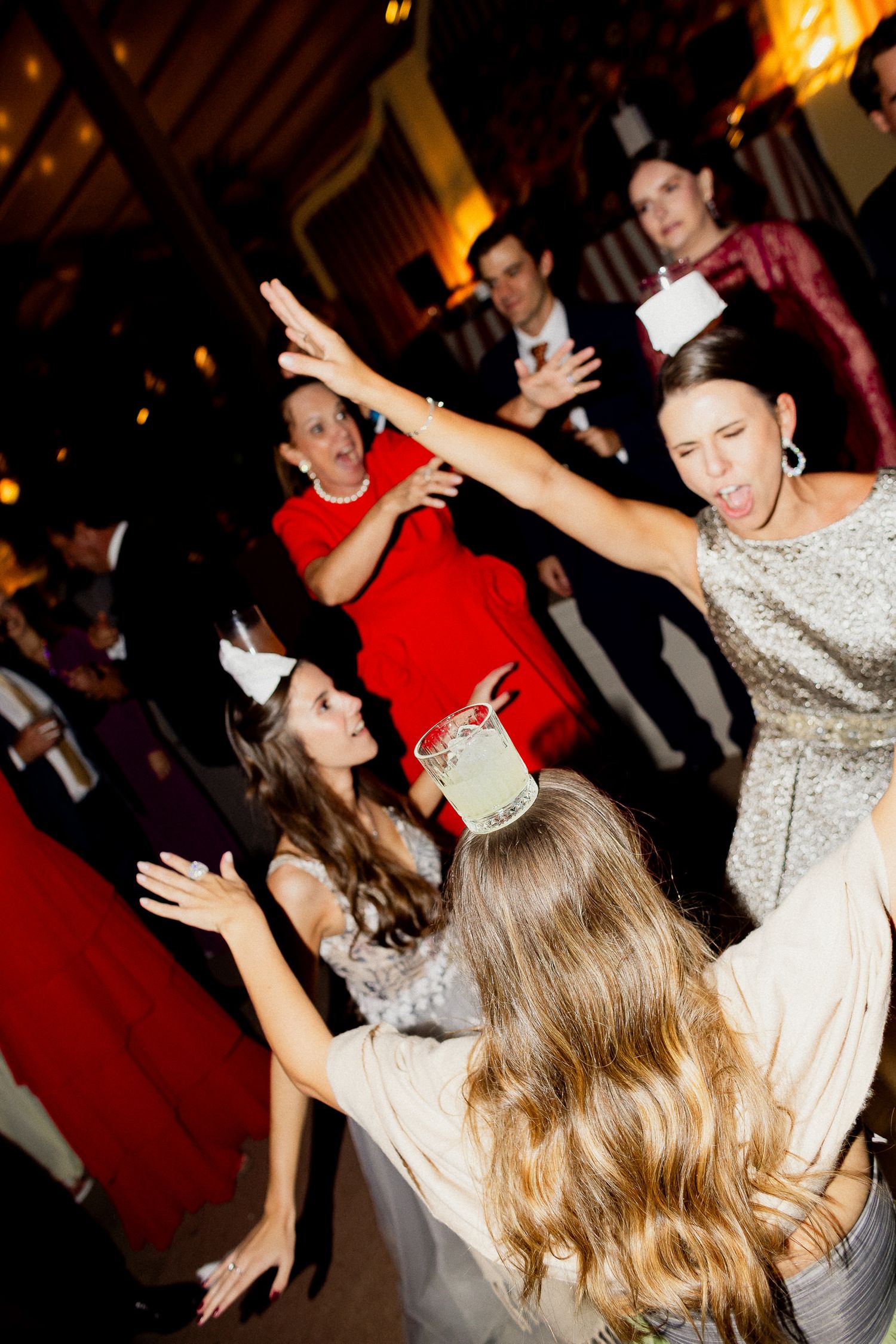 People dancing energetically at a party with their hands raised while colorful lights illuminate the dance floor.